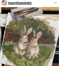 two rabbits are sitting in the grass by some paintbrushes on an easel