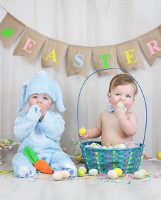 two babies in bunny costumes sitting next to an easter basket