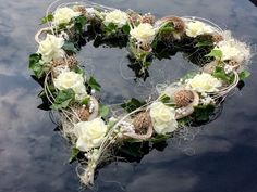 a heart shaped wreath with white flowers and greenery hanging from it's sides