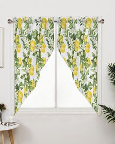 a window with yellow lemons and green leaves on the curtains, next to a potted plant