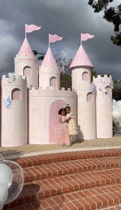 a bride and groom standing in front of a pink castle with balloons on the steps