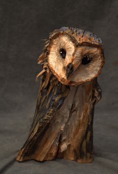 an owl statue sitting on top of a piece of drift wood in front of a gray background