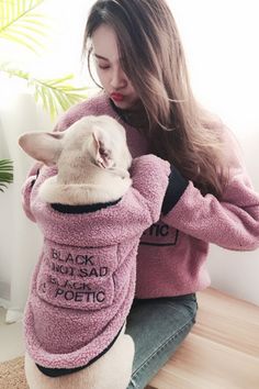 a woman sitting on the floor petting a dog wearing a pink sweater with writing on it