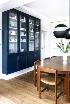 the dining room table is surrounded by dark blue cabinetry and wooden flooring, along with black hanging lights