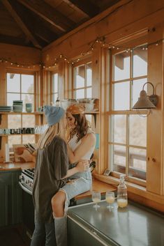 two women standing in a kitchen next to each other and looking out the window together