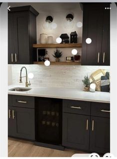 a kitchen with black cabinets and white counter tops, lights above the sink are on