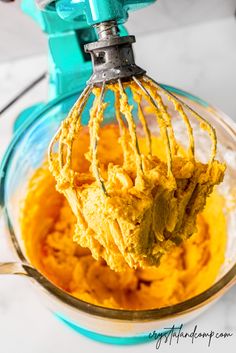 a mixer filled with yellow mashed potatoes on top of a white counter next to a blue blender