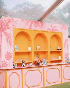 an orange and pink bar with shelves filled with bottles on it's sides in front of a palm tree