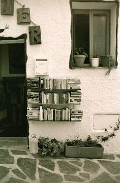 there is a book shelf with many books on it next to a window and potted plants