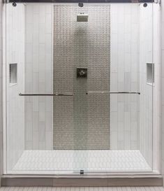 a walk in shower sitting next to a white tiled wall and floor covered in tile