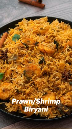 a black plate topped with rice and shrimp next to cinnamon sticks on a wooden table