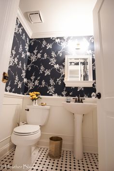 a white toilet sitting next to a sink in a bathroom under a window with blue and white wallpaper