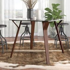 a glass table with four stools and a potted plant in the middle on a rug