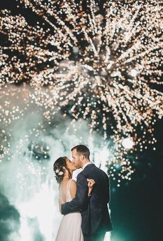 a bride and groom kissing in front of fireworks