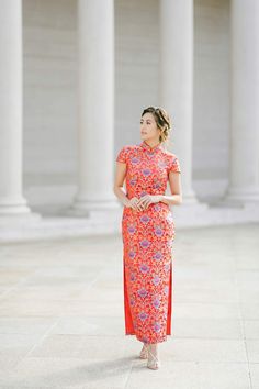 a woman standing in front of columns wearing an orange and pink dress