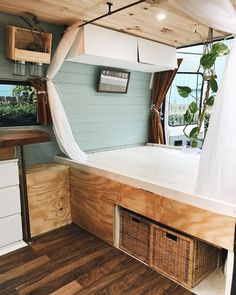 the inside of a camper with wood flooring and white curtains hanging from the ceiling