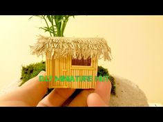 a tiny house made out of bamboo sticks and grass is held by a person's hand