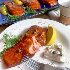 a white plate topped with salmon next to a lemon wedge and whipped yogurt