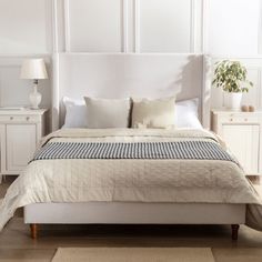 a bed with white linens and pillows in a large room next to two nightstands