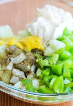 a glass bowl filled with vegetables and seasoning on top of a wooden table next to utensils