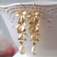 Elegant Gold Orchid Flower Pearl Drop Earrings Each Earring In The Pair Has A White Teardrop Glass Pearl That Dangles At The Bottom Of A Cascade Of Four Increasingly Smaller Gold 14k Plated Orchid Flower Drops. Long Dangling Earrings Feature A Standard Fishhook Closure And Are An Updated And Edgy Version Of The Classic Pearl Earrings That Are Thoroughly Modern. Pair With A White Tee And Jeans, A Minimalist Career Ensemble, Or A Little Black Dress. Pdb 191101a Flower With Pearl Earrings, Boho Bridal Earrings Pearl, Classic Pearl Earrings, Pearl Pendant Earrings, Gold Orchid, Fleur Design, Wedding Party Jewelry, Long Drop Earrings, Pearl Earrings Dangle