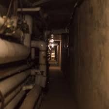 pipes are lined up along the wall in an underground tunnel with light at the end