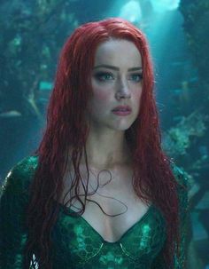 a woman with long red hair and green dress in the shape of a mermaid is looking at the camera