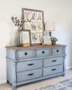 an old dresser is painted blue and has pictures on top, along with flowers in vases