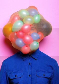 a man with balloons on his head is standing in front of a pink and blue background