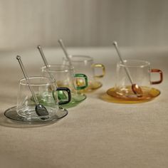 four different colored cups with spoons in them on a tableclothed surface,