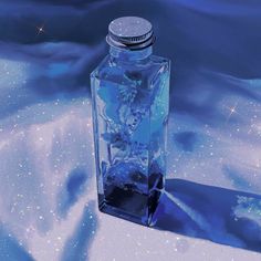 a glass bottle with ice in it sitting on a table next to snow and stars