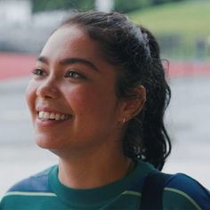 a woman smiling and looking to the side with her hair in a ponytail, wearing a green shirt