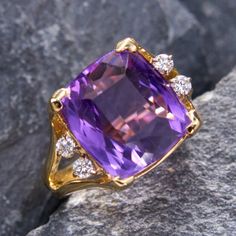 This bold ring is centered with a cushion cut amethyst flanked with four round brilliant cut diamonds and split shoulders. The stones sit a top an angular Euro shank, which helps keep a top heavy ring from spinning. The ring is made of 14k yellow gold and is currently a size 5.5. Please note that one diamond is chipped, but does not affect the beauty of the ring. Luxury Emerald Cut Amethyst Ring For Formal Occasions, Luxury Emerald-cut Amethyst Ring For Formal Events, Luxury Cushion Cut Gemstones With Prong Setting, Luxury Amethyst Ring With Emerald Cut Diamond, Elegant Cushion Cut Gemstones With Prong Setting, Luxury Emerald Cut Amethyst Ring With Diamond Setting, Luxury Emerald-cut Diamond Amethyst Ring, Elegant Cushion Cut Gemstones, Elegant Cushion Cut Gemstone With Center Stone