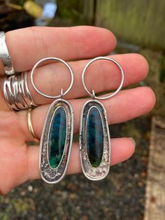 These beautiful pieces of opalized wood are set in sterling silver with a textured and patina'd setting. They will be finished with handmade 1mm sterling silver ear wires.   They measure 61 mm from the top of the hoop to the bottom of the settings. Each piece weighs 6.8g  Colours may vary slightly depending on screen settings. This is a finished piece and cannot be altered. However feel free to message me with any questions or for custom orders. Unique Sterling Silver Jewelry With Patina, Silver Patina Drop Earrings, Handmade Opal Earrings In Silver, Silver Drop Earrings With Patina, Sterling Silver Patina Earrings, Artistic Silver Jewelry With Patina, Solder Jewelry, Opalized Wood, Wood Hoop Earrings