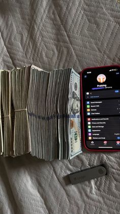 an open cell phone sitting on top of a bed next to stacks of money and a wallet