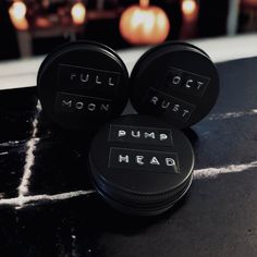 three black buttons that say pumpkin head and full out moon dust on a table with candles in the background