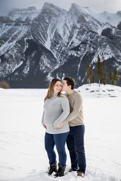 a man and woman standing in the snow with mountains in the backgrouds