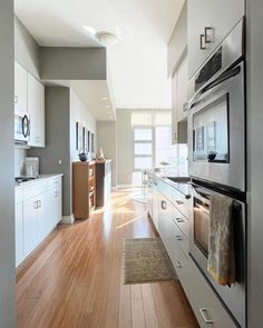 an empty kitchen with white cabinets and wood flooring is seen in this image from the hallway to the living room