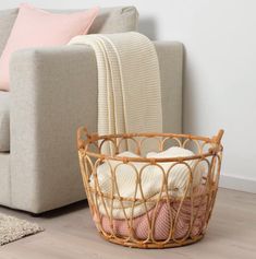 a wicker basket sitting on the floor next to a couch with blankets in it