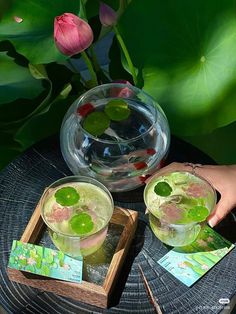 two glasses filled with green liquid sitting on top of a wooden table next to flowers