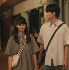 a man and woman standing next to each other on a sidewalk in front of buildings