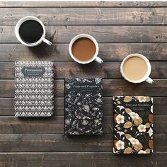 two cups of coffee and three books on top of a wooden table next to each other