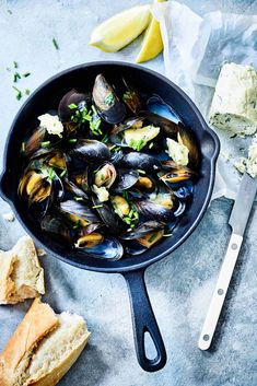 a pan filled with mussels next to bread and butter on top of a table