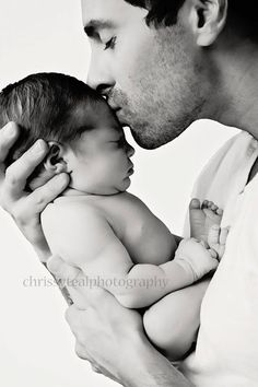 a man holding a baby in his arms and kissing it's face with the other hand