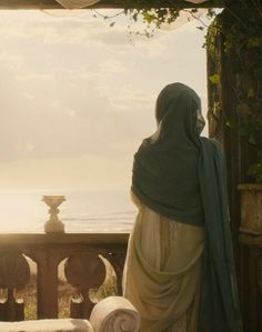 a woman sitting on a bench looking out at the ocean from an outside balcony area