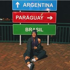 a woman is sitting on the ground in front of street signs that read argentina, paraguay and brasil