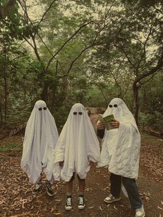 three people dressed in white ghost costumes standing on a path with trees and bushes behind them