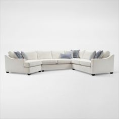 a white sectional couch with pillows on the top and bottom corner, in front of a plain background