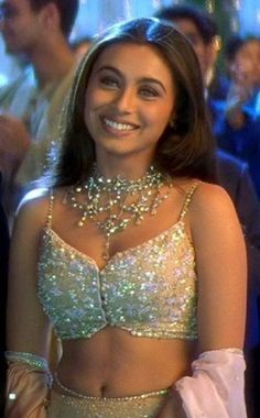 a woman in a silver bra top and skirt with jewels on her chest smiling at the camera