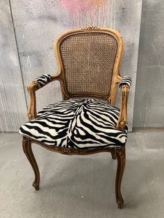 an old chair with zebra print upholstered on the seat and back, in front of a graffiti covered wall